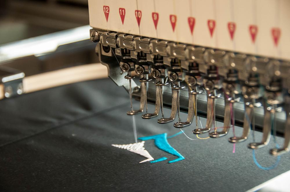 Embroidery machine stitching a dense multi-colour logo design into fabric